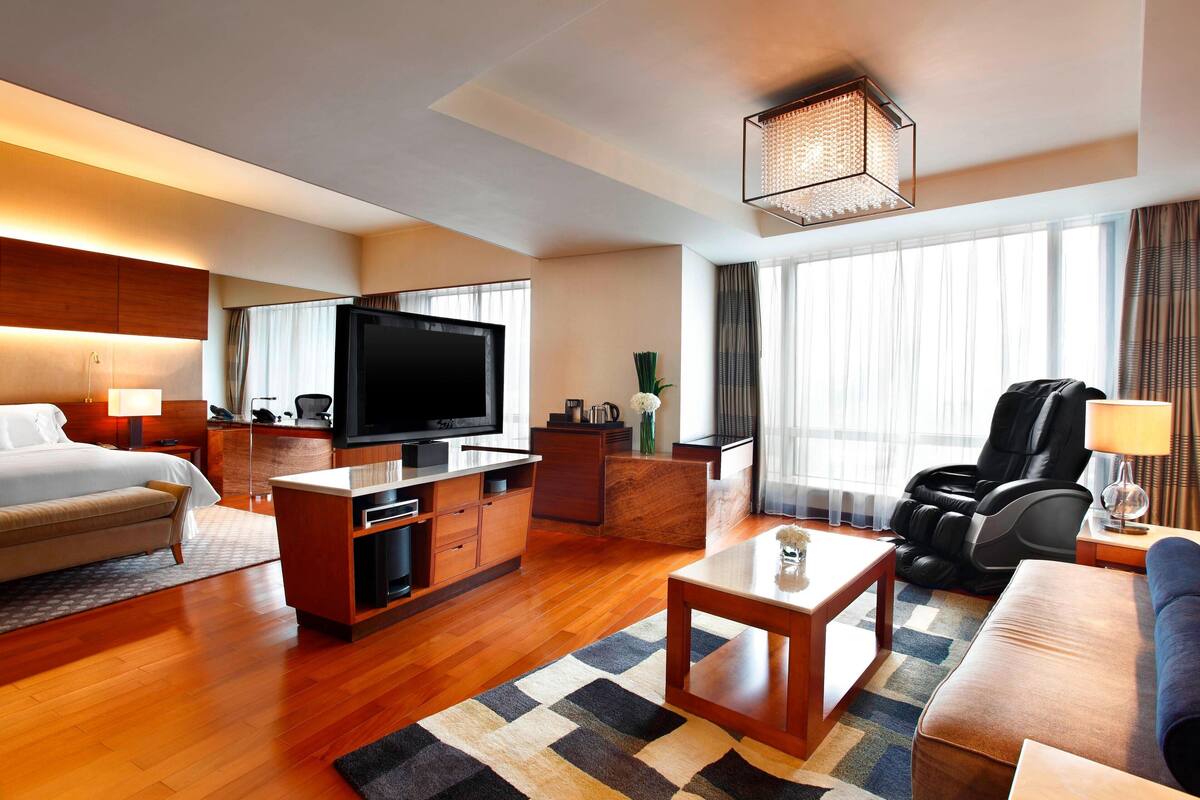 A modern hotel room with a bed, a TV, a massage chair, and a coffee table.
