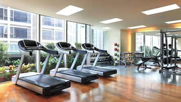 Un gimnasio con cintas de correr, máquinas de pesas y un amplio ventanal con vistas a edificios.