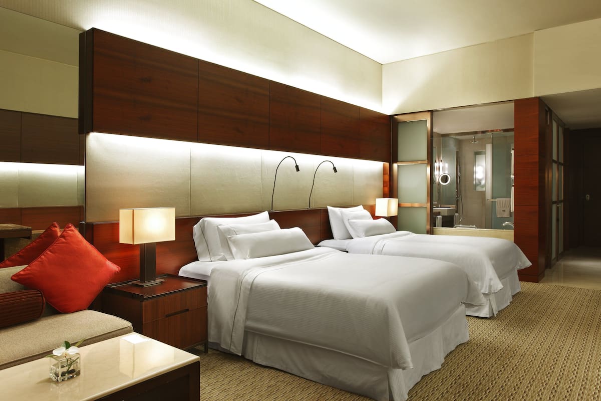 A hotel room with two beds, a nightstand with a lamp, a small table with a vase, and a mirror.