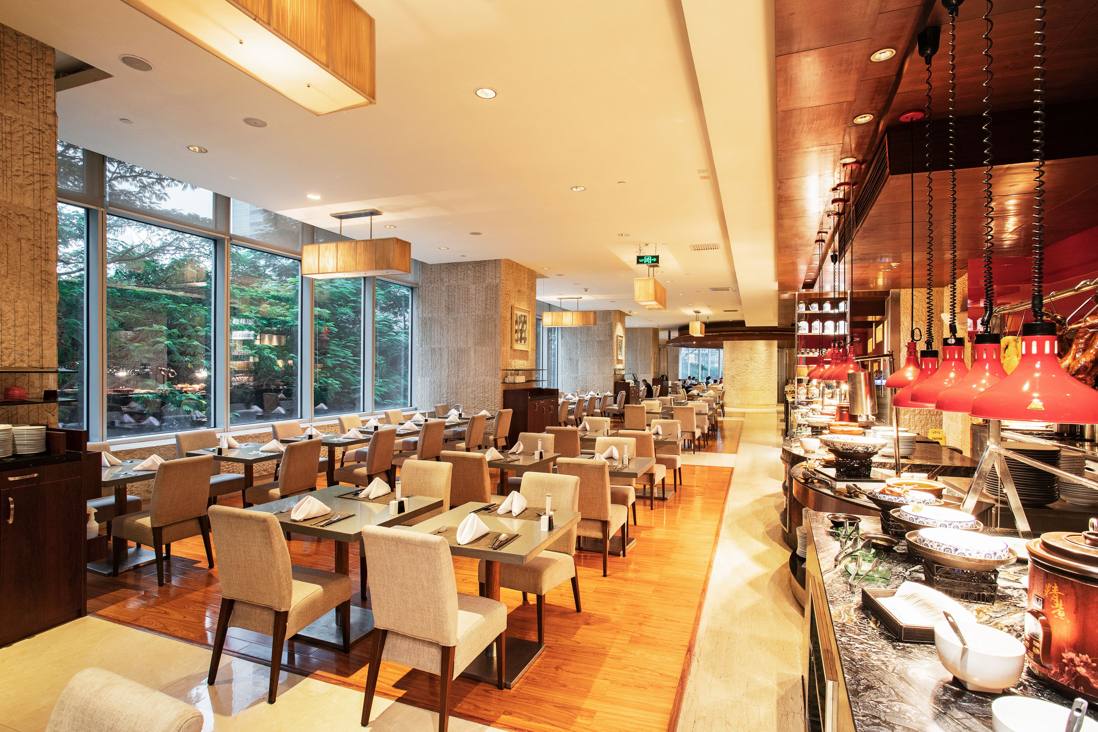 A spacious restaurant with high ceilings, large windows, and a buffet area.