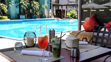 A poolside table with drinks and a coconut, overlooking a swimming pool.