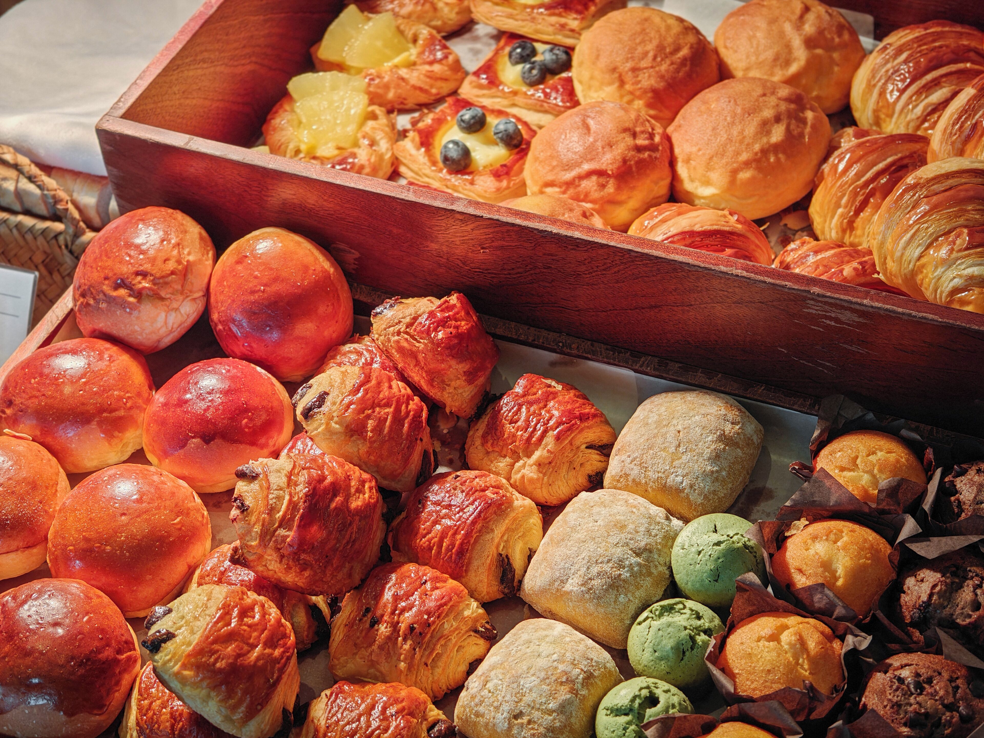 Variedad de productos horneados, como pasteles, pan y muffins, expuestos en cajas de madera.