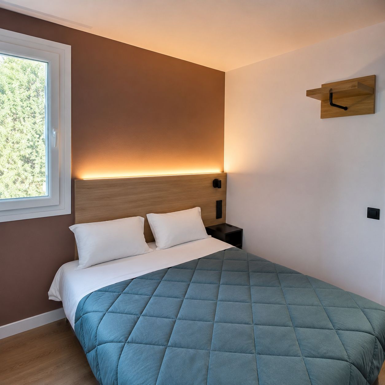 A bedroom with a bed, a bedside table, a wall-mounted clock, and a window.