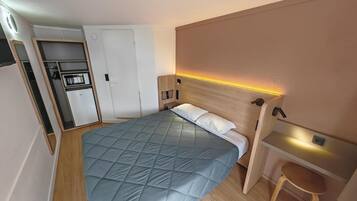 A compact bedroom with a bed, a small desk, and a built-in wardrobe.