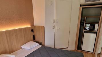 A hotel room with a large bed, a wardrobe, a microwave, and a refrigerator.
