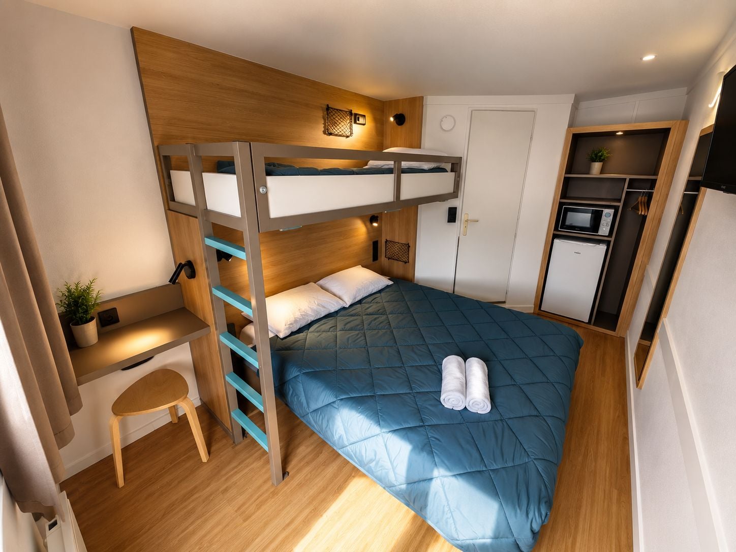Una cama individual con escritorio y silla, microondas y refrigerador en una habitación pequeña.