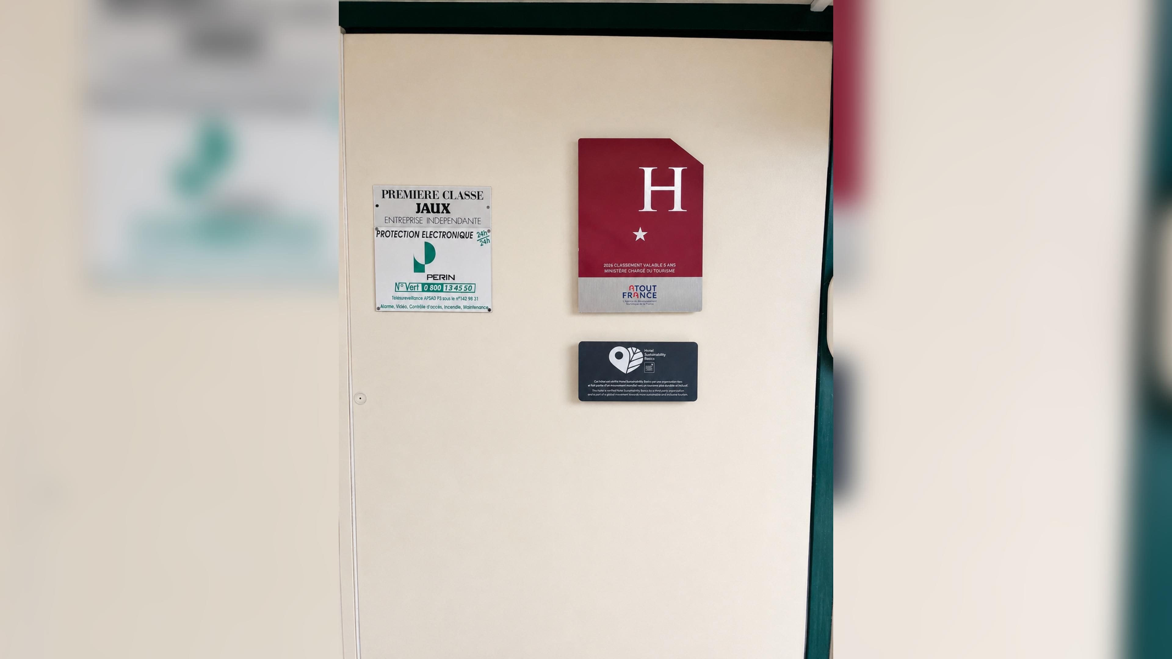 A door with a sign indicating a first-class hotel, a red card with a white 'H' and stars, and a black card with a sustainability logo.