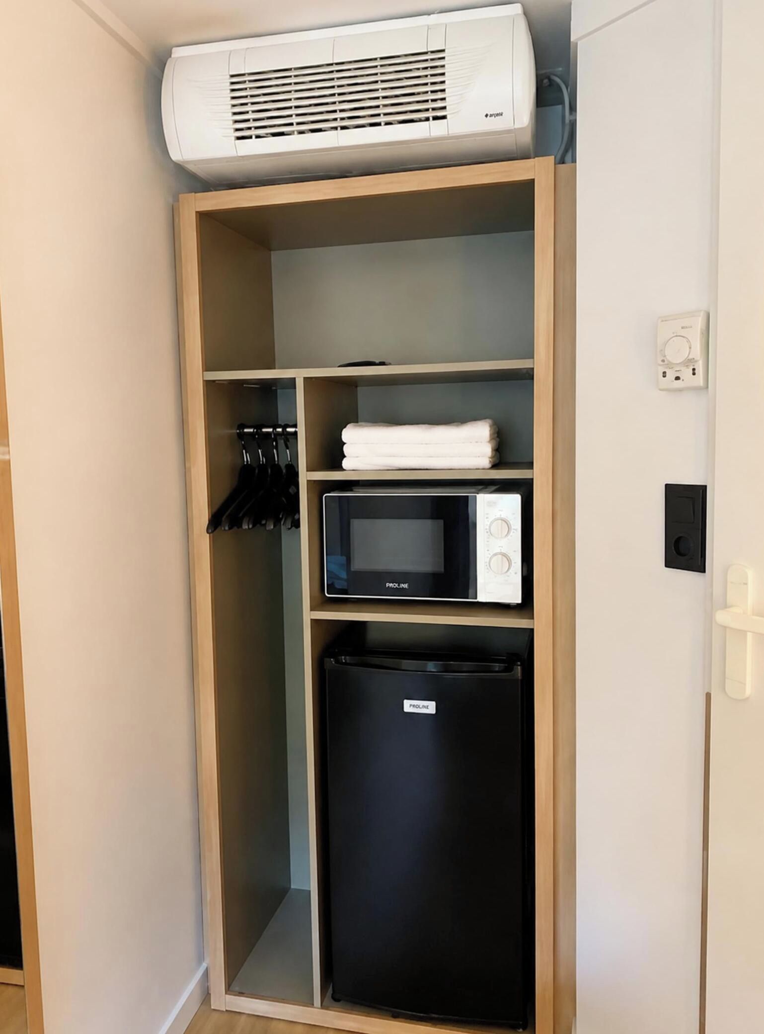 A compact kitchenette with a built-in air conditioner, a microwave, and a refrigerator.