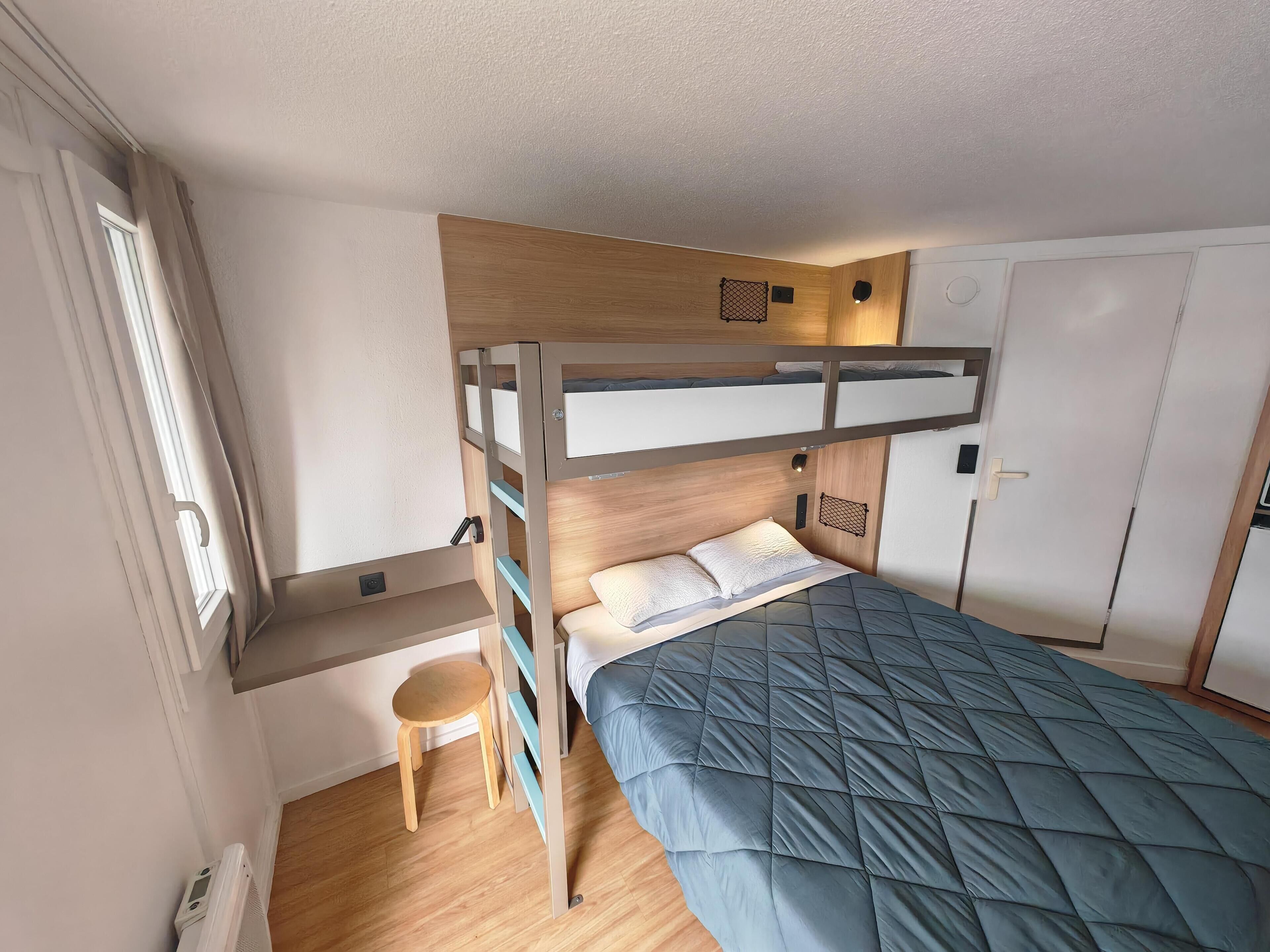 Un lit superposé avec un bureau et une chaise, une armoire et un petit tabouret.