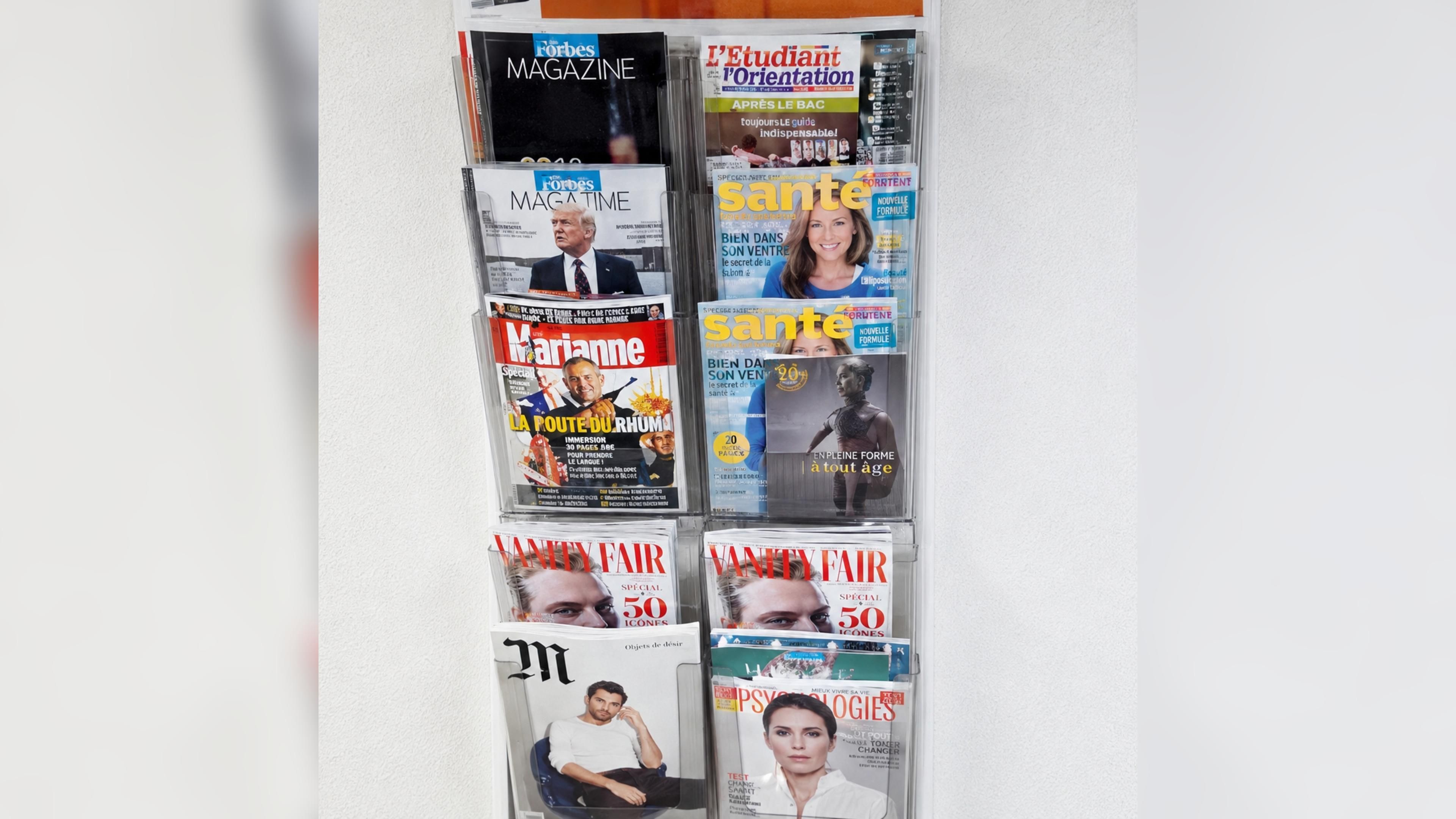 A wall with various magazines and newspapers, including titles like Forbes, Marie, and Vanity Fair.