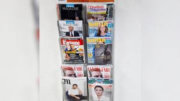 A wall with various magazines and newspapers, including titles like Forbes, Marie, and Vanity Fair.