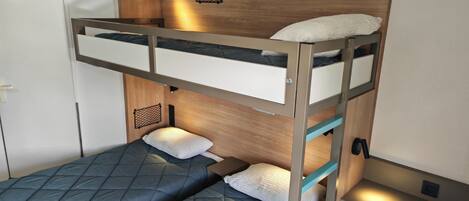 A bunk bed with a wooden headboard, a small shelf, and a wall-mounted light fixture.