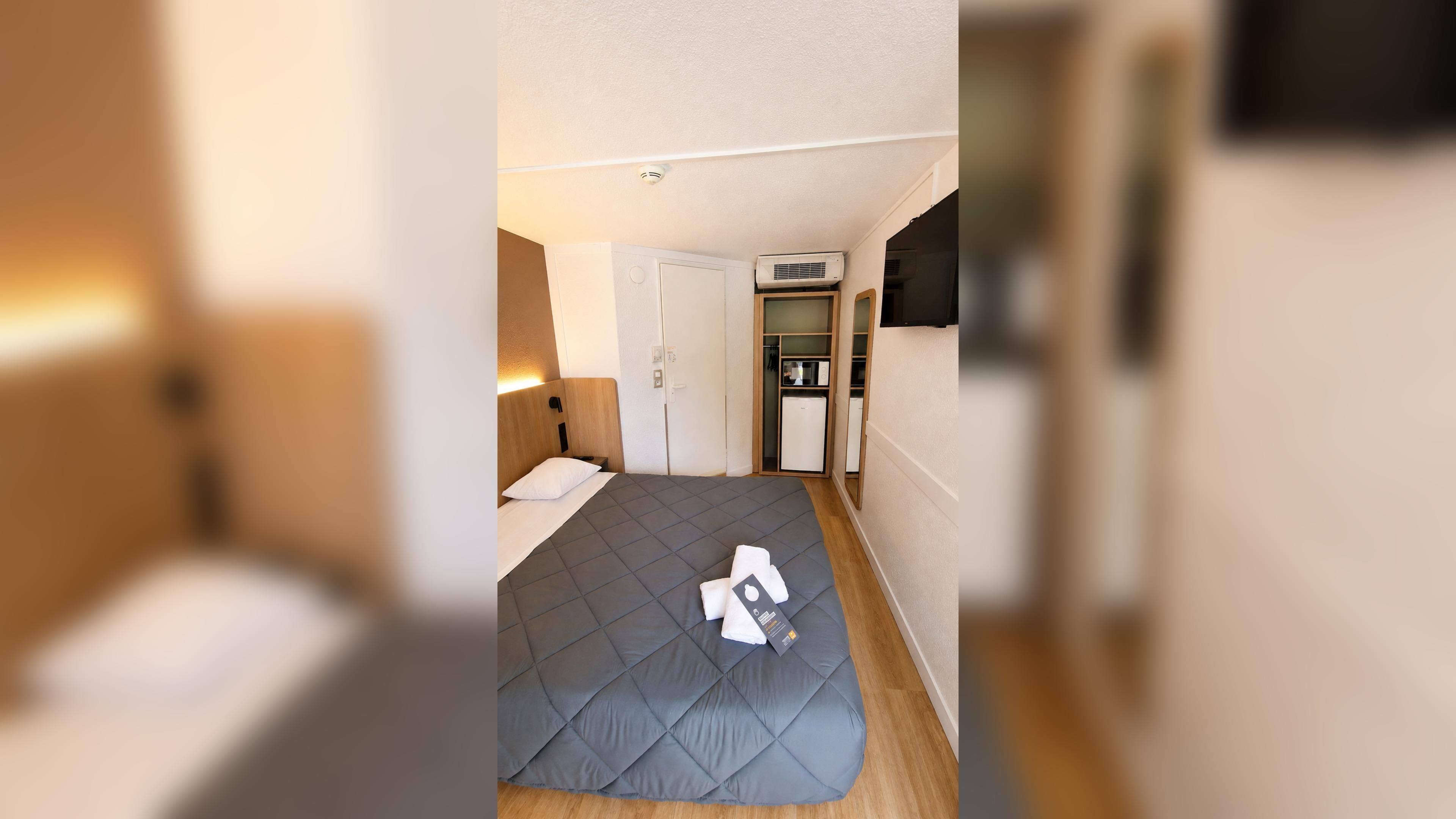 Ein kleines Hotelzimmer mit Bett, einer Küchenzeile und einem Kleiderschrank.
