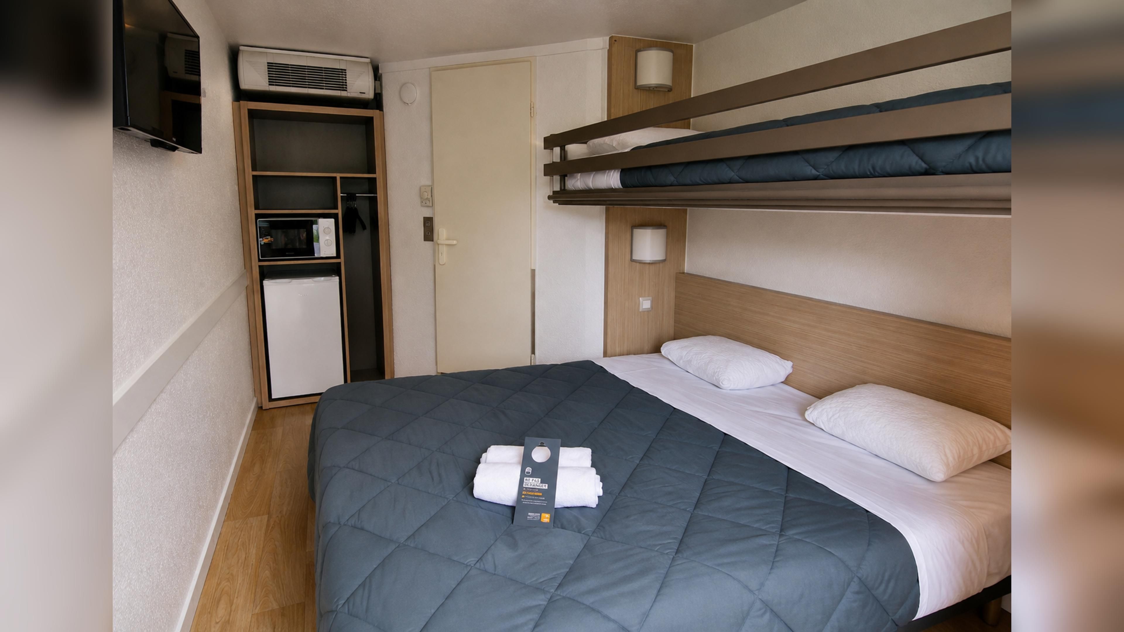 Una camera d'albergo compatta con letti a castello, angolo cottura e TV a schermo piatto.