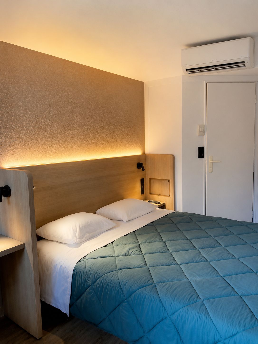 Une chambre d’hôtel comprenant un lit, des tables de chevet, un appareil de climatisation et une porte.