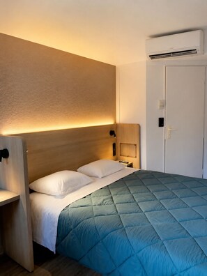 A hotel room with a bed, bedside tables, an air conditioning unit, and a door. - Premiere Classe Compiègne - Jaux (Jaux)