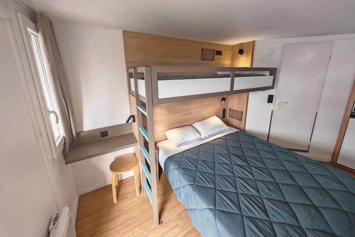 Habitación con literas, un escritorio, una silla, un armario y un taburete pequeño.