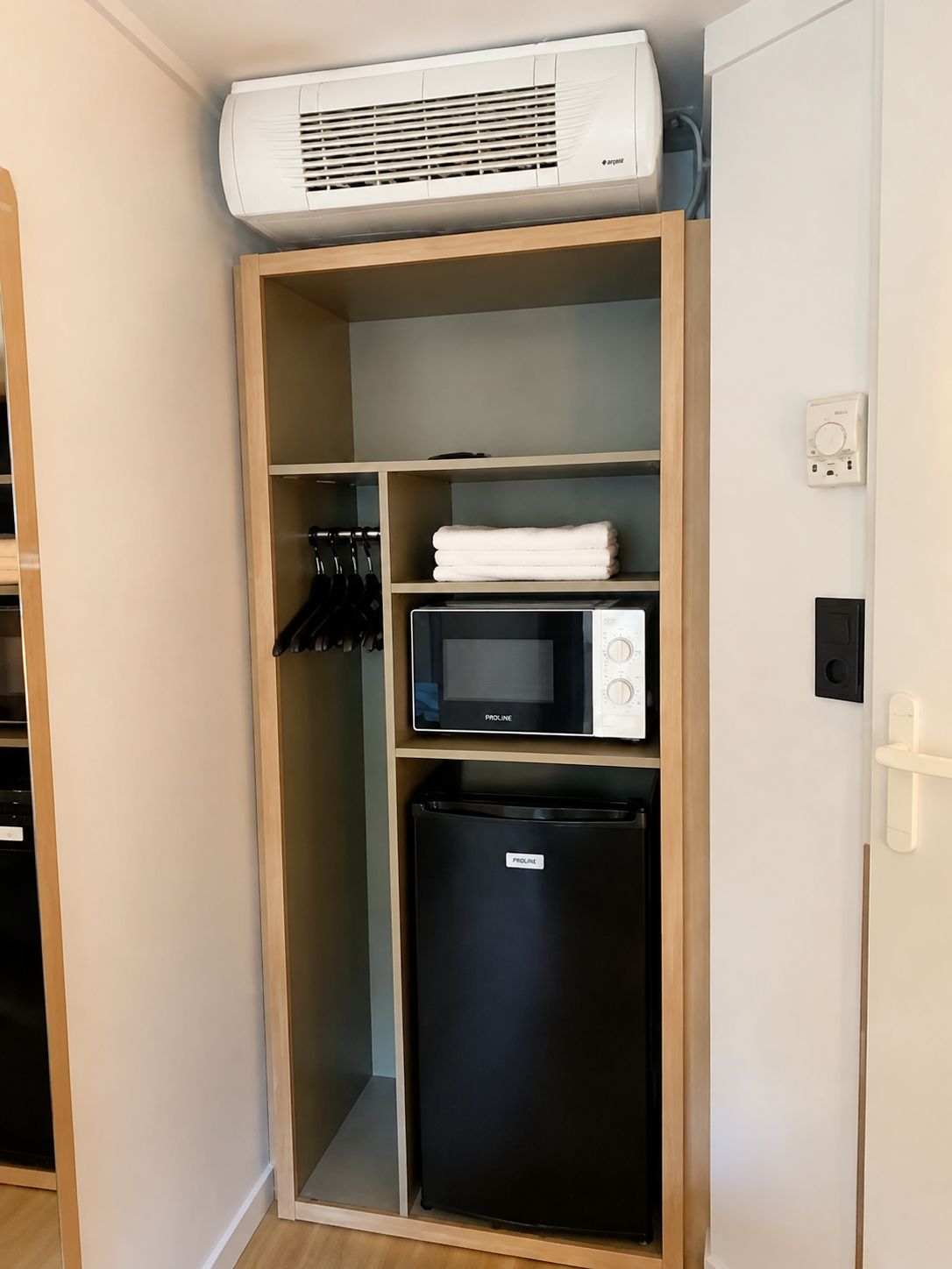 Een compact keukenhoekje met een ingebouwde magnetron, een koelkast en een wandairconditioning.