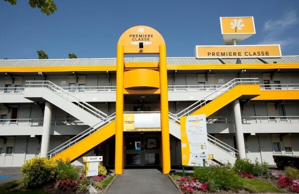 Fachada de hotel con un llamativo esquema de colores amarillo y blanco, un letrero que dice "HOTEL PREMIERE CLASSE" y una escalera que conduce a la entrada.