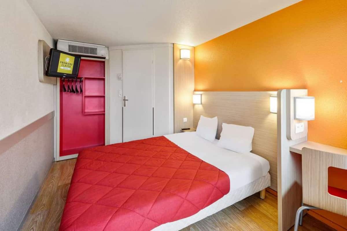 Ett hotellrum med en säng, ett skrivbord, en garderob och en tv.