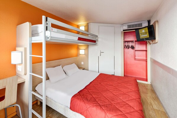 Una cama literera con colcha roja, un escritorio, una silla, un televisor y un armario.