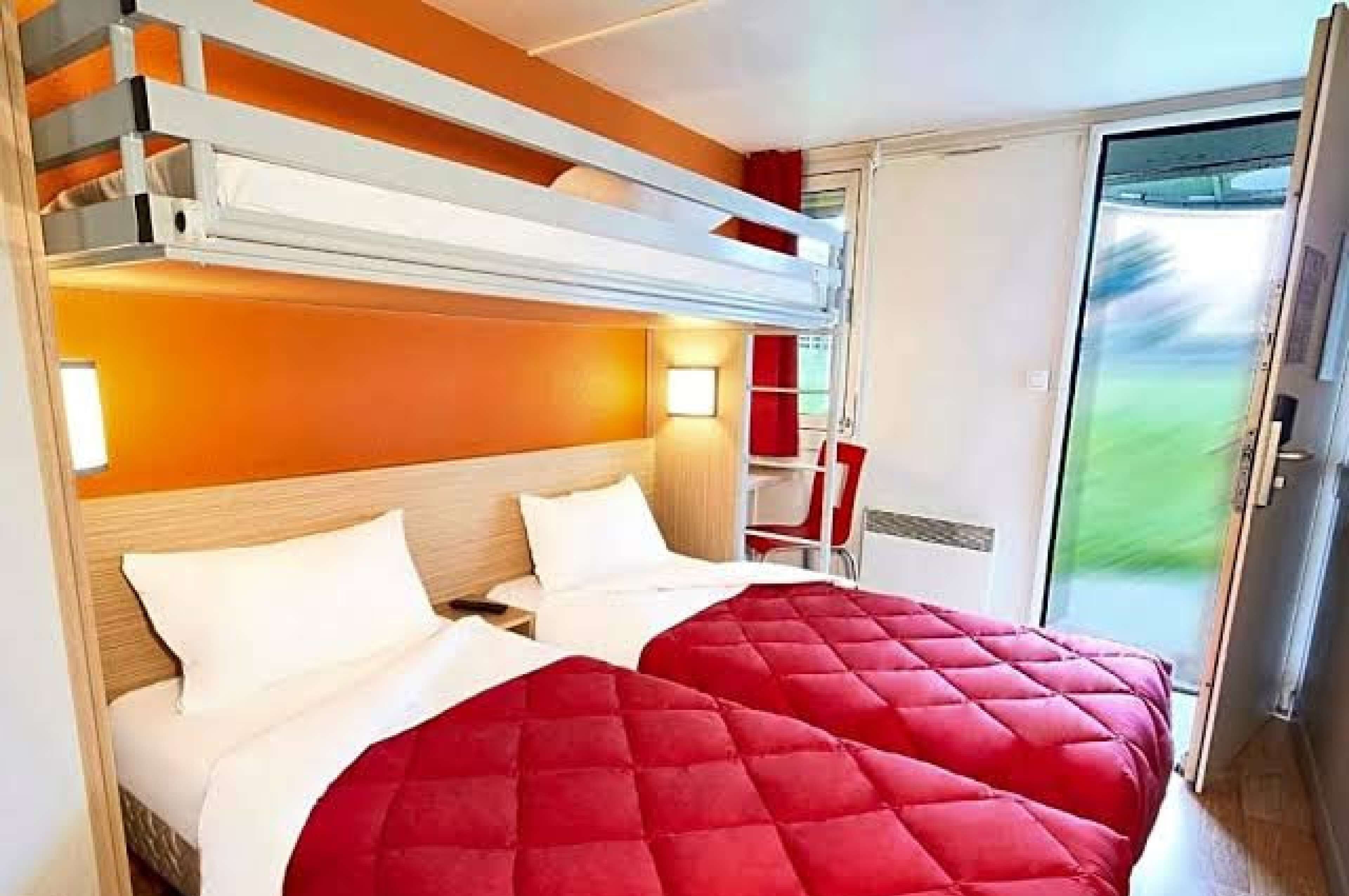 Une chambre d’hôtel avec un lit superposé, un bureau et une porte coulissante donnant sur un balcon.