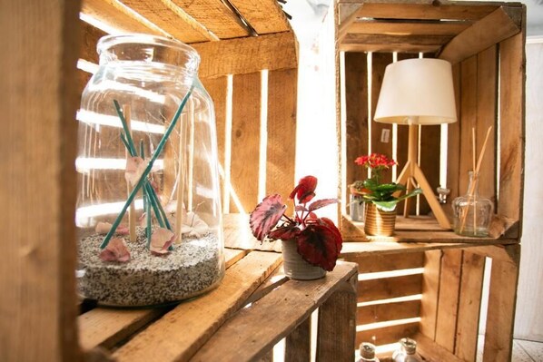 A rustic wooden shelf with a glass terrarium, a red potted plant, a lamp, and a small figurine.