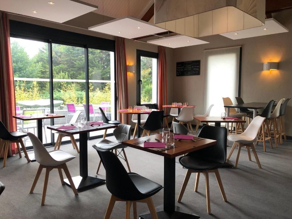 Un comedor moderno con mesas y sillas, ventanas amplias y vistas a la vegetación exterior.