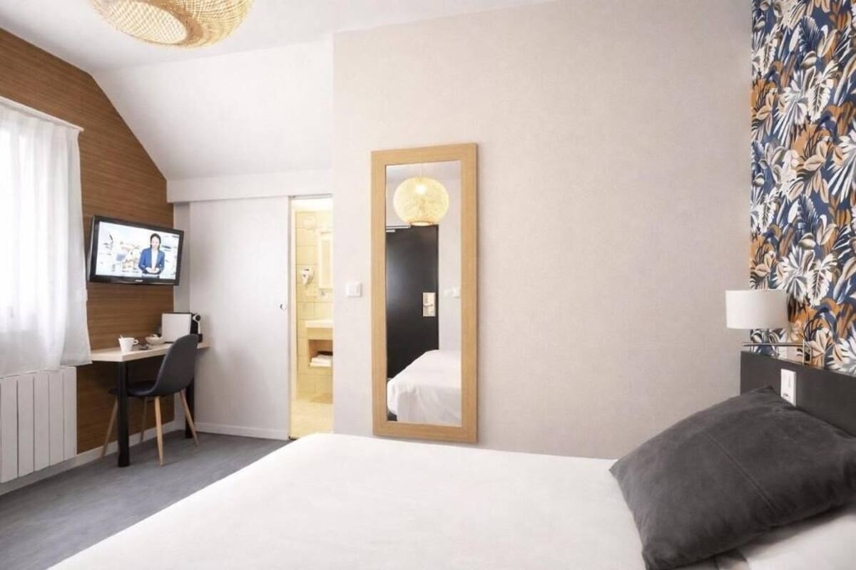 Een hotelkamer met een bed, een bureau, een televisie, een spiegel en een behang met patroon.