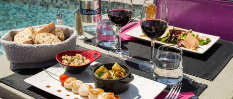 A dining table with a variety of dishes, including seafood, a bowl of bread, and a bottle of water, set against a poolside view.