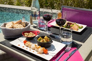 A dining table with a variety of dishes, including seafood, a bowl of bread, and a bottle of water, set against a poolside view. - Logis Hôtel Au Chêne Vert (Plerin)