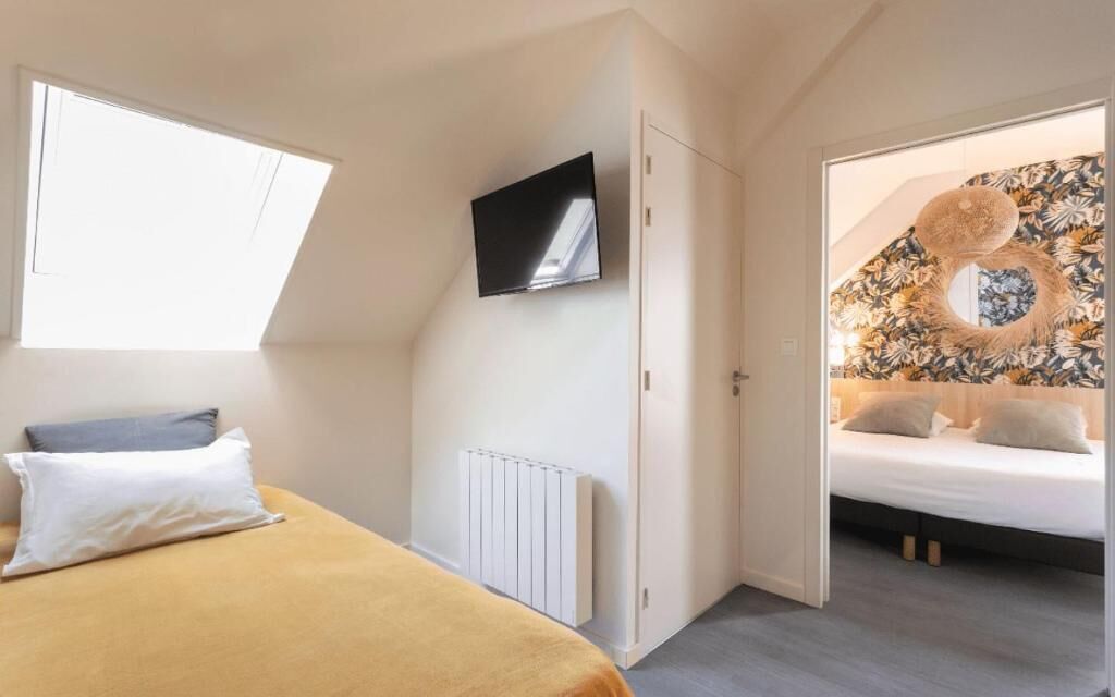 A bedroom with a bed, a TV mounted on the wall, a radiator, and a window.
