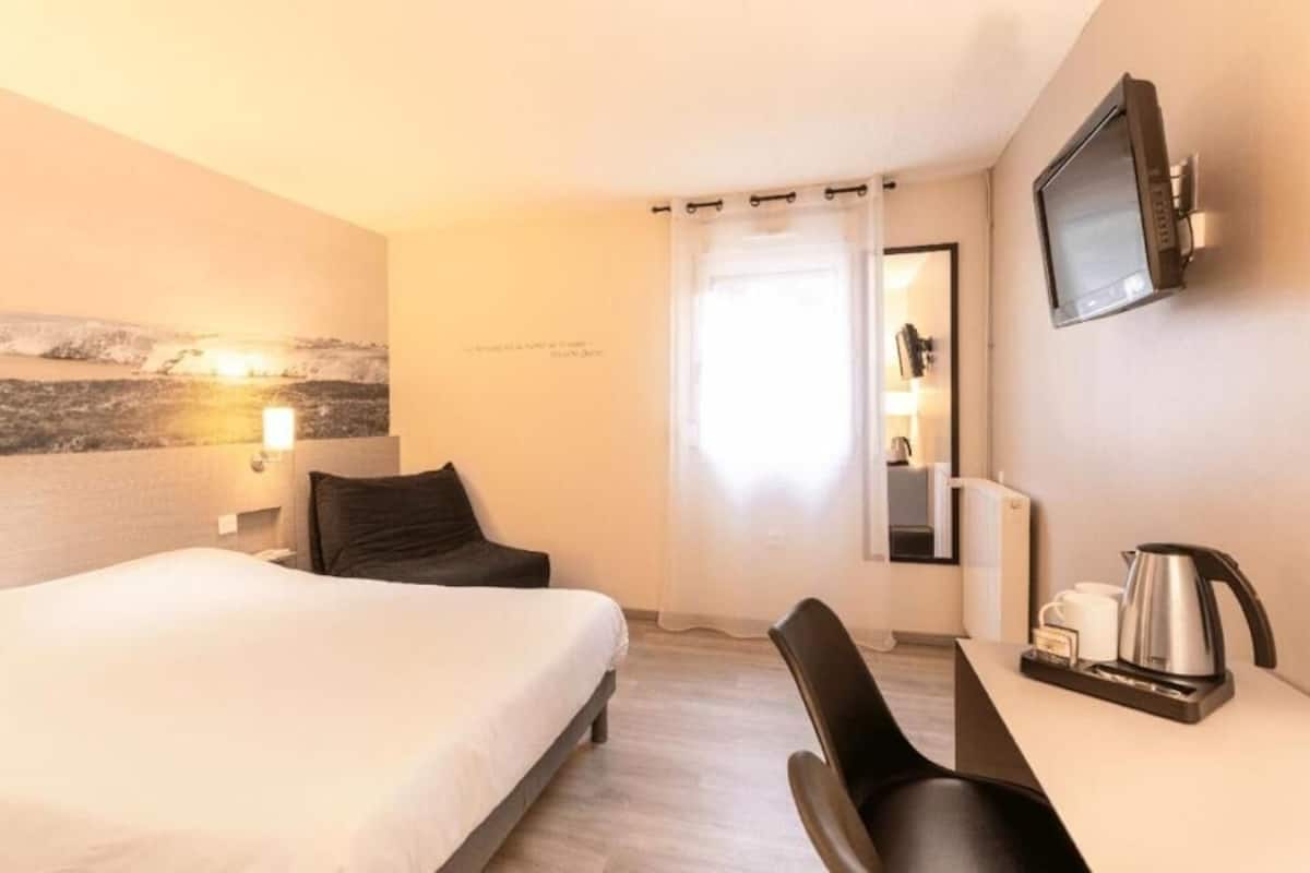 Een hotelkamer met een bed, een bureau met stoel, een televisie en een koffiezetapparaat.