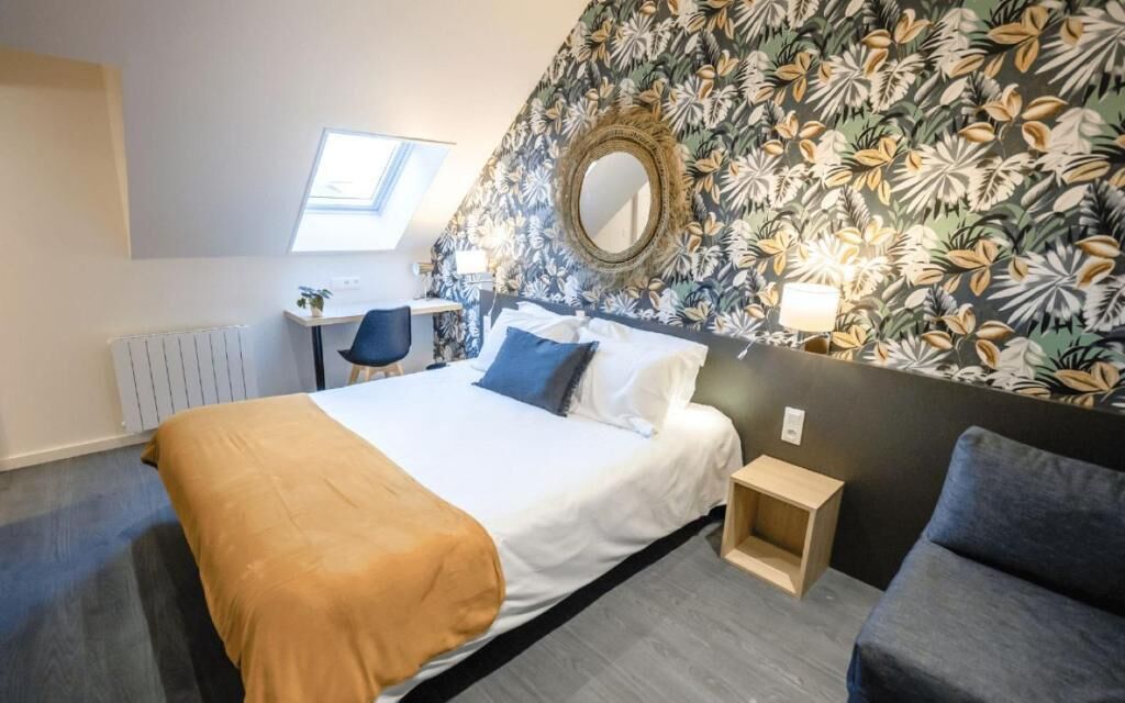 Habitación de hotel con cama, escritorio, silla, sofá, espejo y ventana.