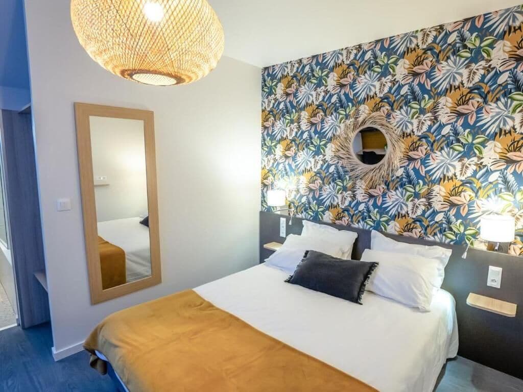 Une chambre d’hôtel avec un lit, un grand miroir, un mur orné d’un motif floral et un élément décoratif circulaire placé au-dessus du lit.