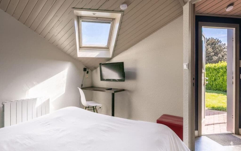 Une chambre avec un puits de lumière, un lit, un bureau, une chaise et un téléviseur.