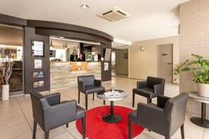 A lobby with a reception desk, black leather chairs, a red rug, and a potted plant. - Logis Hôtel Au Chêne Vert (Plerin)