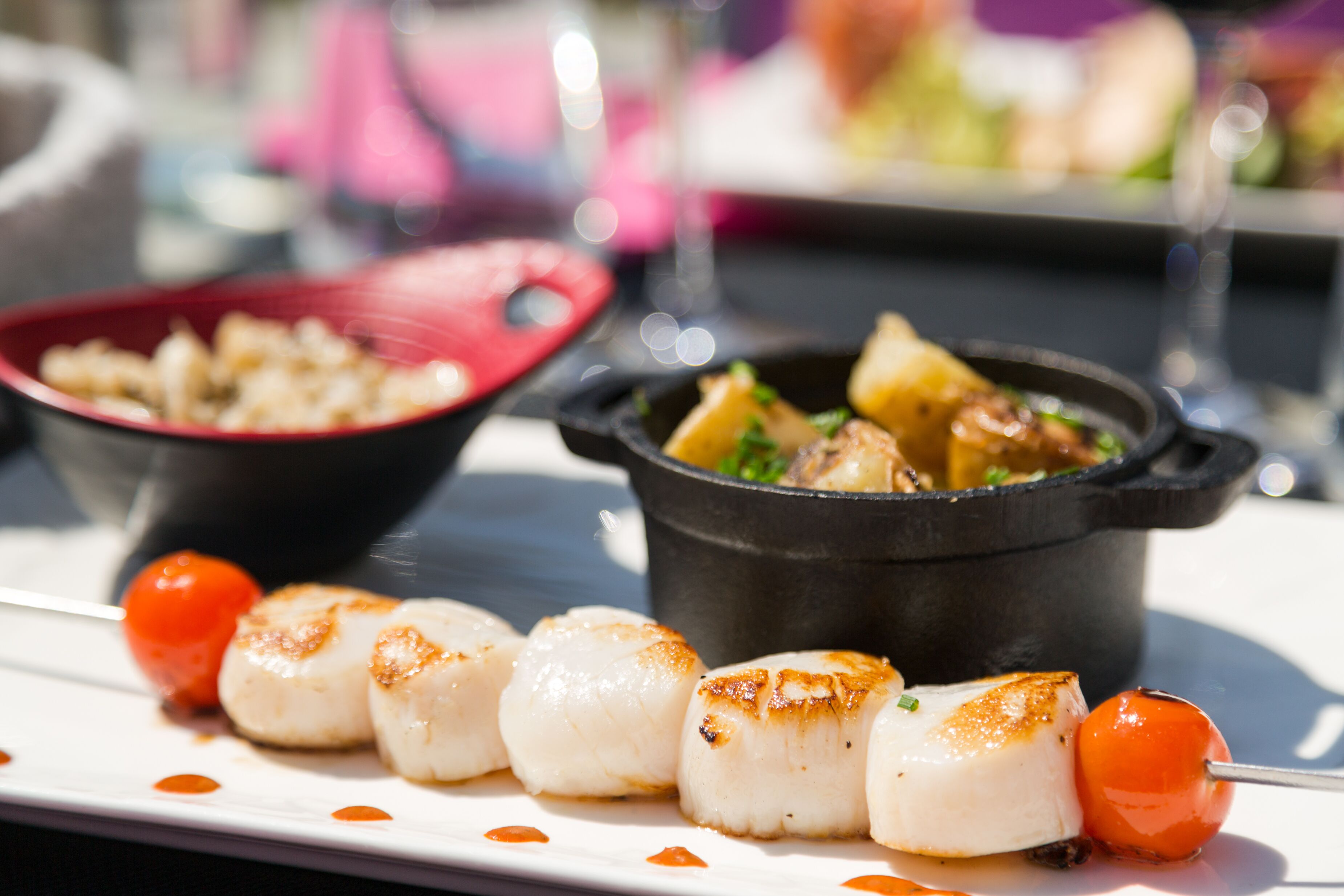 A plate with seared scallops and cherry tomatoes, a bowl of salad, and a pot of stew.