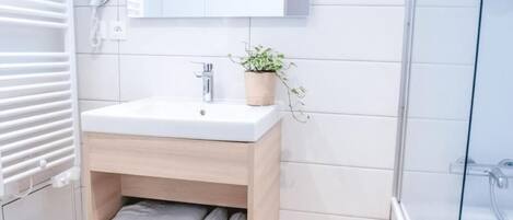 A modern bathroom with a white sink, wooden vanity, and a glass shower enclosure.