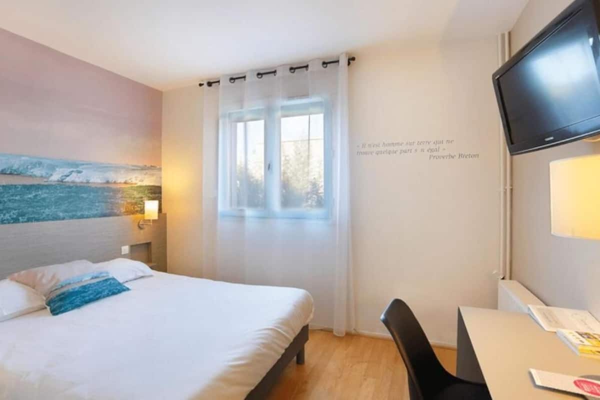 Een hotelkamer met een bed, een bureau, een stoel, een televisie en een raam met gordijnen.