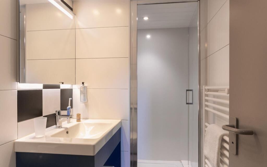 Een moderne badkamer met een grote spiegel, een wastafel en een douchecabine met glazen wanden.
