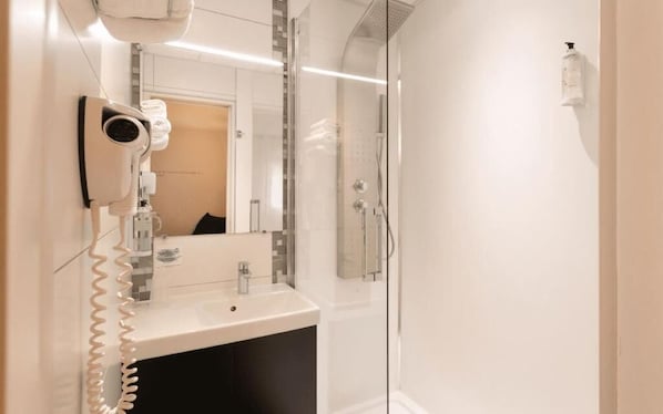A modern bathroom with a hairdryer, a sink, and a glass shower enclosure. - Logis Hôtel Au Chêne Vert (Plerin)
