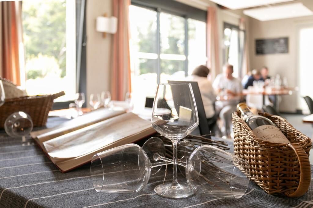 Un coin repas avec une table mise pour le dîner, des verres à vin et un panier rempli de bouteilles de vin.