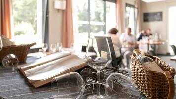 Un coin repas avec une table mise pour le dîner, des verres à vin et un panier rempli de bouteilles de vin.