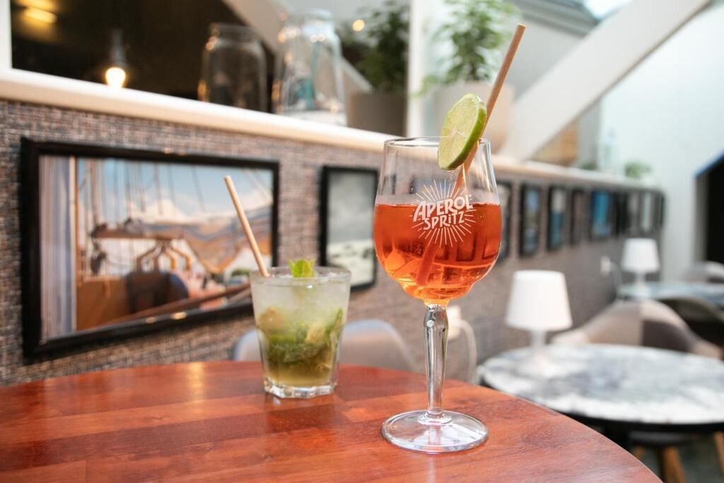 Two drinks on a wooden table with a framed picture in the background.