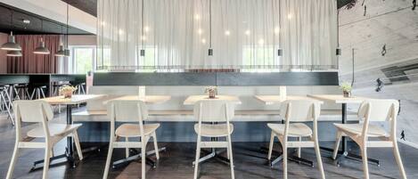 A modern restaurant with a long counter, white chairs, and pendant lighting.