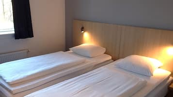 A hotel room with two beds, a headboard with integrated lighting, a window with curtains, and a visible ceiling vent.