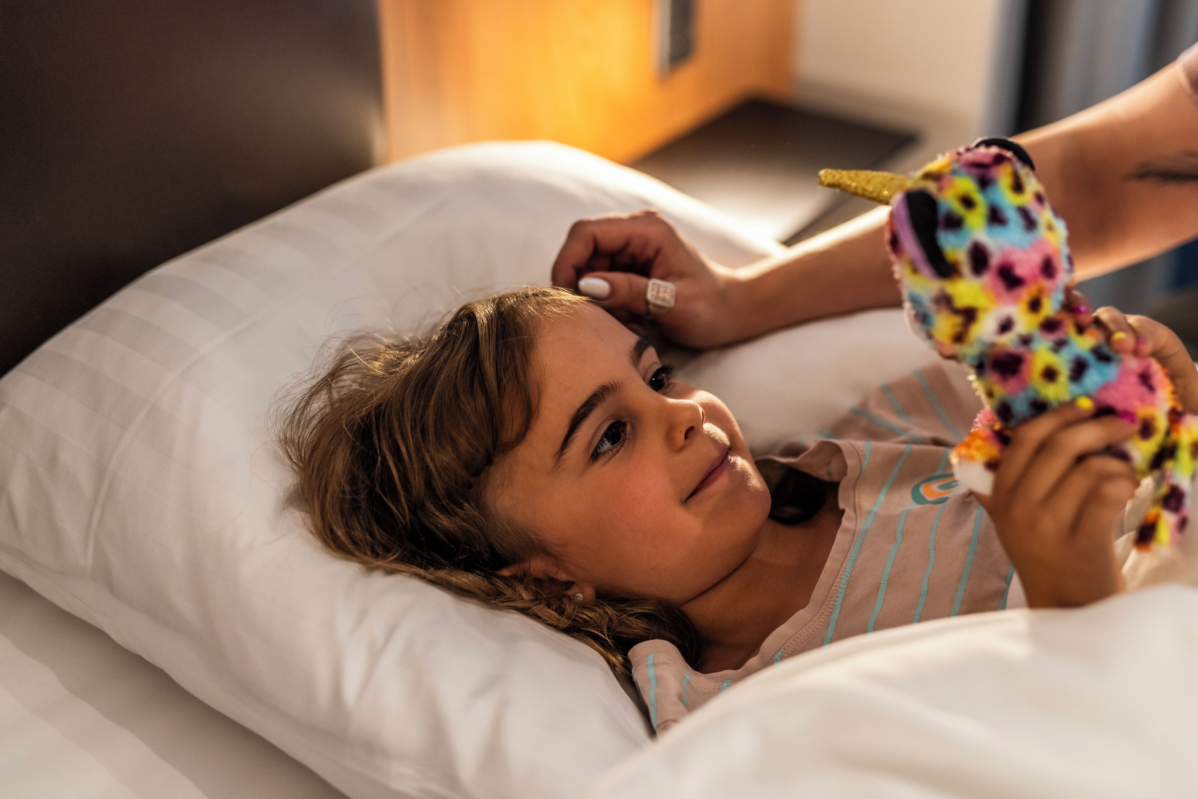 Una persona acostada en la cama con un peluche colorido.