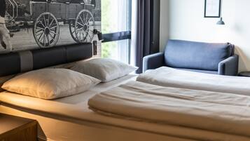 A hotel room with a bed, two pillows, a chair, a nightstand, and a window with curtains.