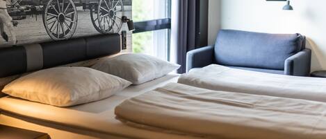 A hotel room with a bed, two pillows, a chair, a nightstand, and a window with curtains.